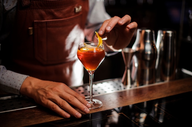 Barman avec verre et zeste de citron prépare un cocktail au bar