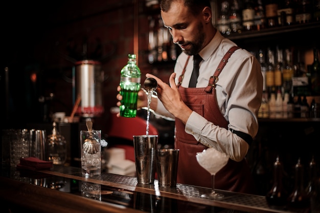 Barman versant un achohol de la tasse à mesurer dans un shaker en acier