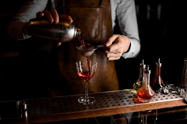 Barman Versant Une Boisson Alcoolisée Rouge Du Shaker En Acier à Travers Le Tamis