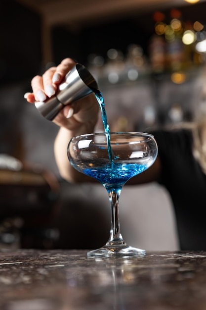 Un barman versant une boisson bleue dans un verre à martini