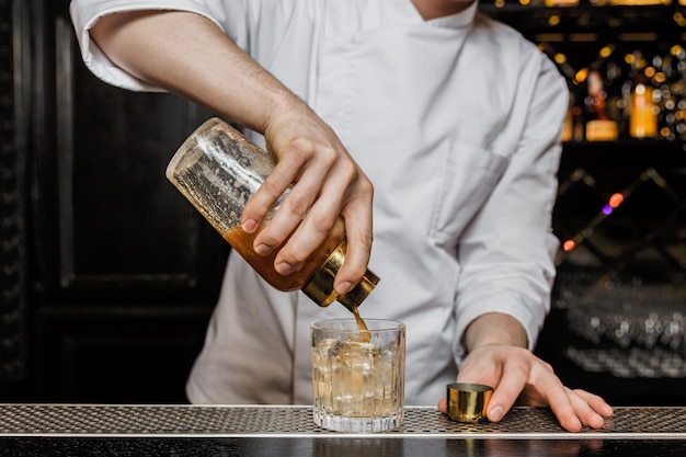 Barman versant un verre d'un shaker dans un verre à whisky.