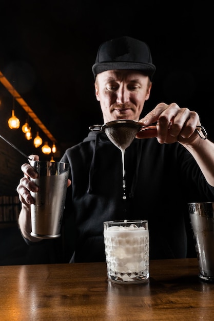 Le barman verse un cocktail de pénicilline mélangé dans le verre au bar Le barman mélange du jus de citron au whisky et du sirop de gingembre pour préparer le cocktail alcoolisé de pénicilline
