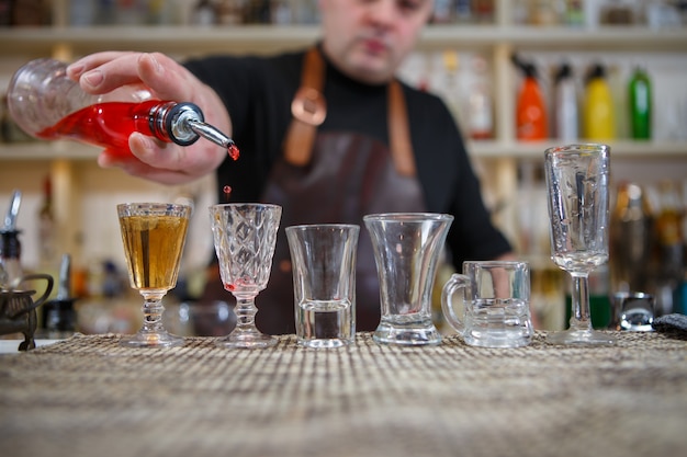 Le barman verse diverses boissons alcoolisées dans de petits verres sur le bar