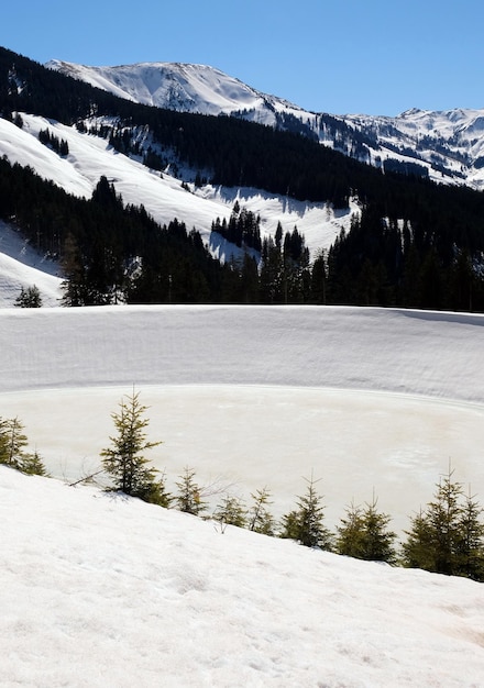 Un barrage d'un lac gelé dans les montagnes enneigées avec des arbres sous un ciel bleu ensoleillé en hiver