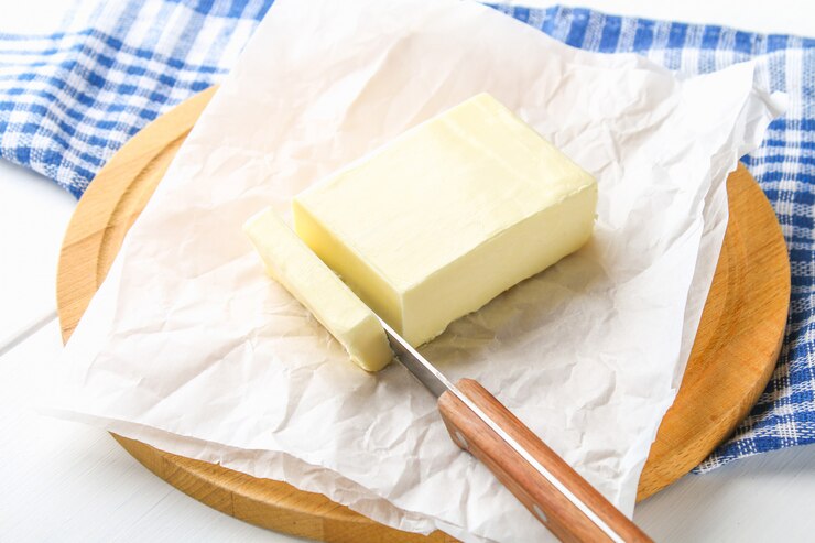 Une barre de beurre sur une planche de bois avec un couteau, sur une table blanche. Ingrédients pour la cuisine
