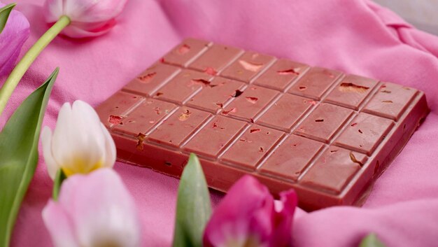 Photo une barre de chocolat rubis rose avec des fraises séchées surgelées sublimées et des amandes et des tulipes de printemps