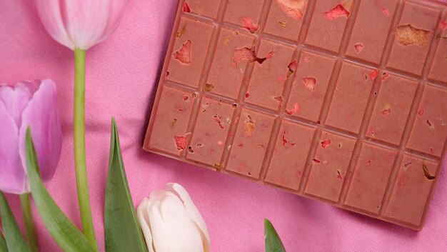 Photo une barre de chocolat rubis rose avec des fraises séchées surgelées sublimées et des amandes et des tulipes de printemps