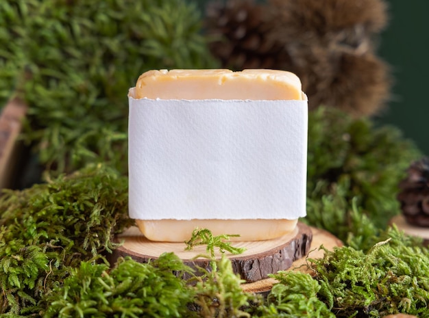 Photo barre de savon avec étiquette vierge sur un morceau de bois près de la mousse verte en gros plan maquette cosmétique naturelle