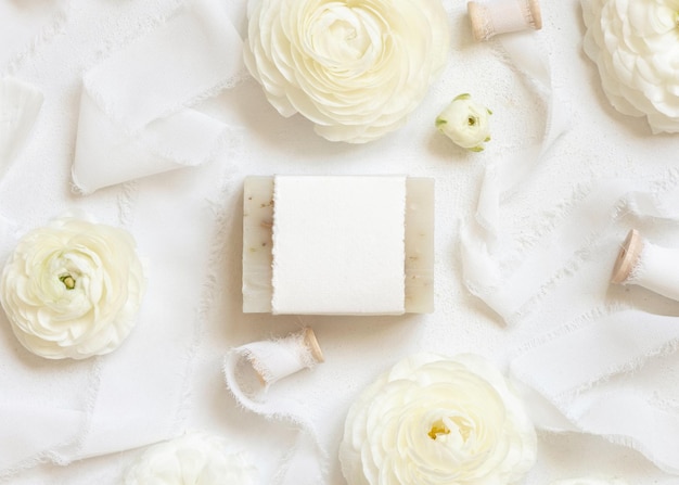 Barre de savon faite à la main avec étiquette vierge près de roses crème et maquette de vue de dessus de rubans blancs