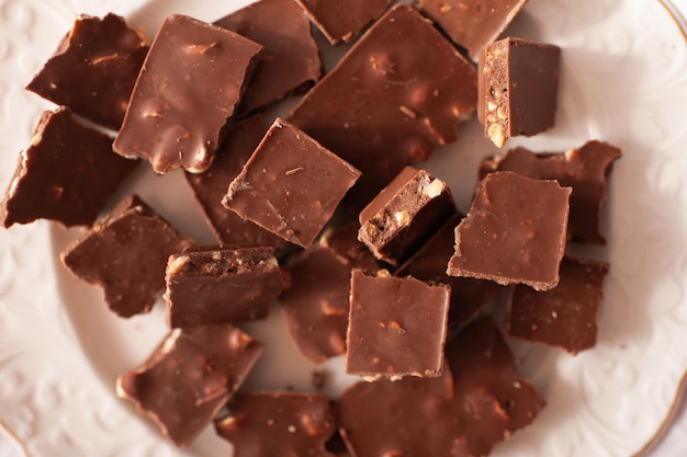 Barres de chocolat hachées avec des noix sur une plaque blanche se bouchent. Vue de dessus.