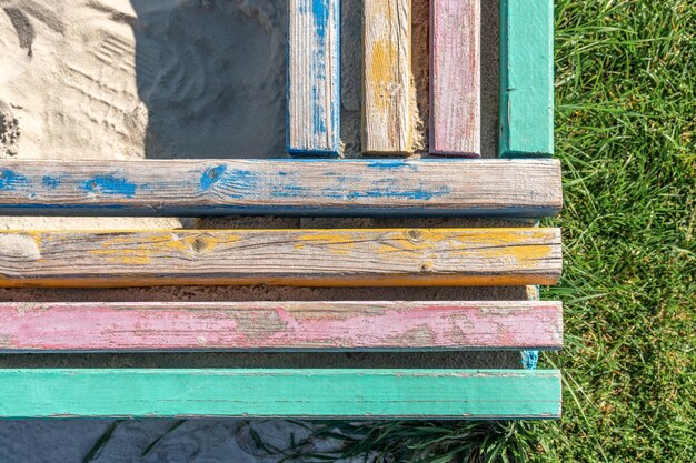 Photo barrière en béton avec des barres de bois colorées servant de sièges entourant une sable pour enfants