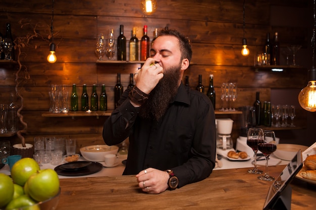 Bartende mangeant une délicieuse pomme verte derrière le comptoir du bar. Homme élégant.