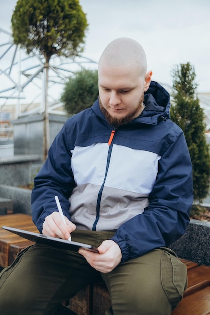 D'en bas d'un homme hipster utilisant une tablette moderne avec un stylet tout en créant un nouveau projet et assis dans la rue