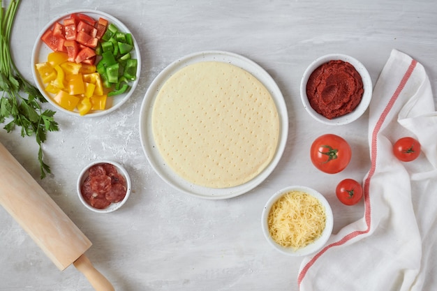 Base de pizza de pâte fraîche et ingrédients sur un tableau blanc