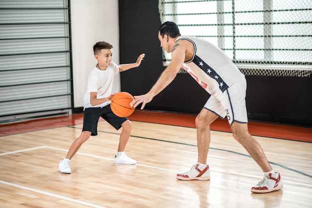 Basketball. Homme aux cheveux noirs entraînant un adolescent dans la salle de sport