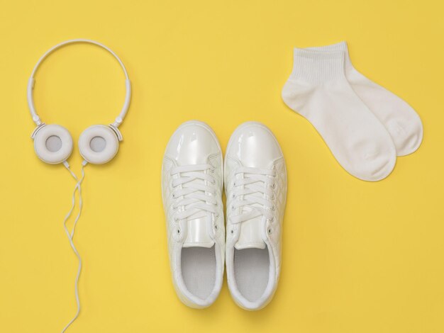 Baskets blanches écouteurs blancs et chaussettes de sport blanches sur fond jaune Le concept d'un mode de vie sain et de la musique