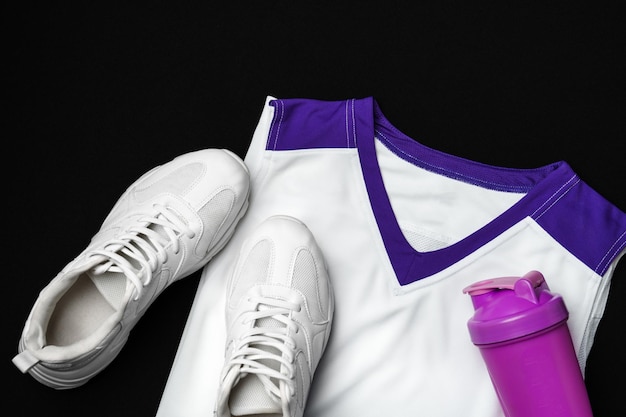 Des baskets blanches avec un tank top violet et une bouteille de shaker sur un fond noir