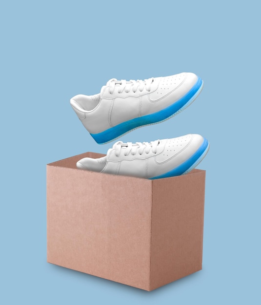 Des baskets en cuir blanc sortent d'une boîte en carton sur un fond bleu