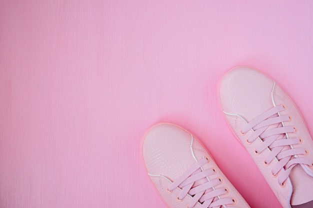 Baskets féminines roses sur fond rose. Appartement plat, fond minimal, vue de dessus.