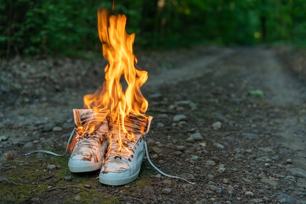 Baskets hautes blanches usagées sur une route rurale et un incendie