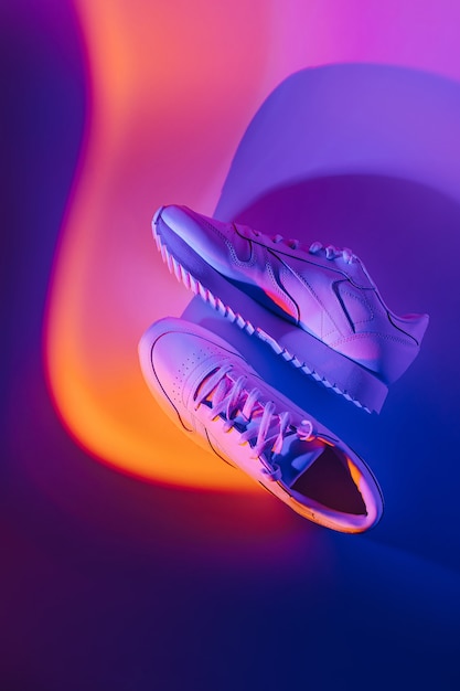 Baskets mode sur fond abstrait vif. Chaussures de sport en néon. Dégradé violet et orange.