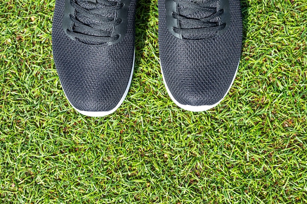 Baskets noires pour hommes avec semelles blanches gros plan sur l'herbe verte artificielle.