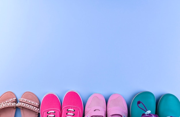 Baskets roses, bottes en caoutchouc et sandales pour fille sur fond bleu. Chaussures différentes.