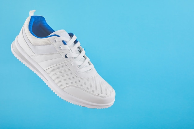 Des baskets de sport blanches lévitent sur un fond bleu. Baskets homme élégantes pour le fitness.