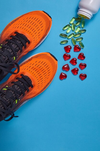 Photo des baskets de sport orange et des capsules jaunes de vitamine d et des cœurs de verre rouge sont éparpillés sur un fond bleu.