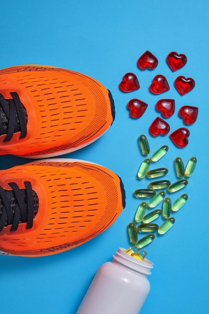 Des baskets de sport orange et un pot avec des capsules d'acides gras polyinsaturés et des cœurs décoratifs sur un fond bleu