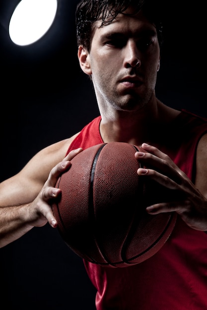 Basketteur avec un ballon dans ses mains et un uniforme rouge. studio de photographie.