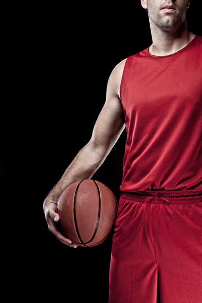 Basketteur avec un ballon dans ses mains et un uniforme rouge. studio de photographie.