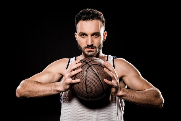 Basketteur sérieux tenant le ballon isolé sur noir
