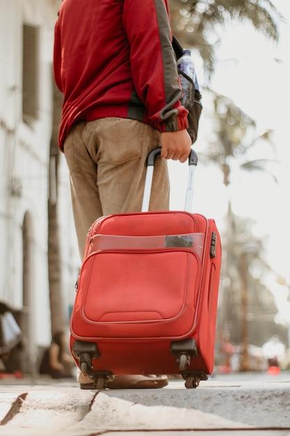 Photo basse section de l'homme debout avec des bagages sur le trottoir