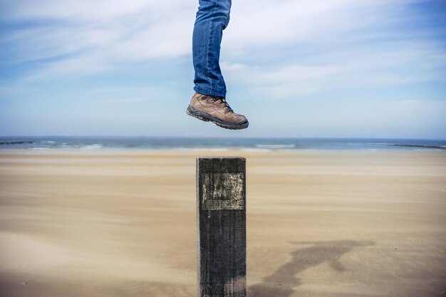 Basse section de l'homme sur un poteau de bois sur la plage contre le ciel