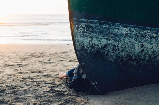 Photo basse section d'une personne assise par bateau amarré à la plage