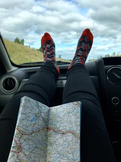 Photo basse section de la personne avec la carte reposant les jambes sur le tableau de bord dans la voiture