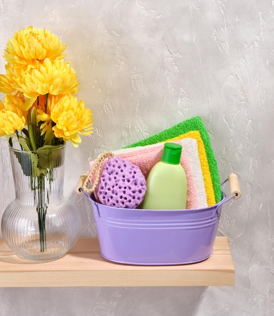 Bassin en métal violet avec gel douche, serviettes de douche fraîches et éponge de douche Fleurs jaunes printanières dans un vase