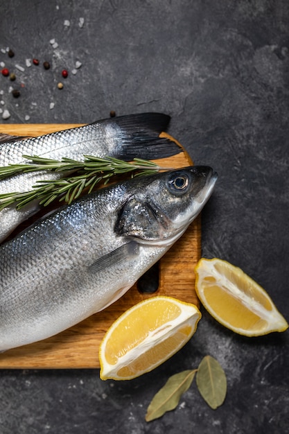 Bassin de poisson frais et ingrédients pour la cuisine, citron et romarin. Vue de dessus de fond sombre.