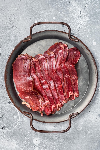 Basturma en tranches de viande de boeuf séchée dans un plateau en acier Fond gris Vue de dessus