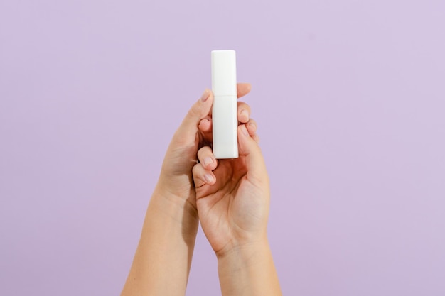 Bataille de crème cosmétique dans la main de la femme sur fond lilas clair Concept de beauté Tube d'emballage pour produits cosmétiques