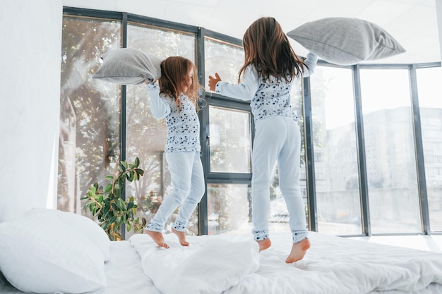 Bataille d'oreillers Deux jolies petites filles à l'intérieur à la maison ensemble Enfants s'amusant