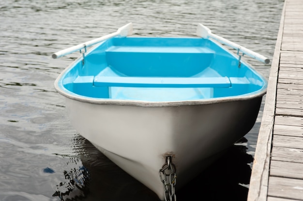 Un bateau bleu et blanc avec des rames se dresse sur l'eau à une jetée en bois.