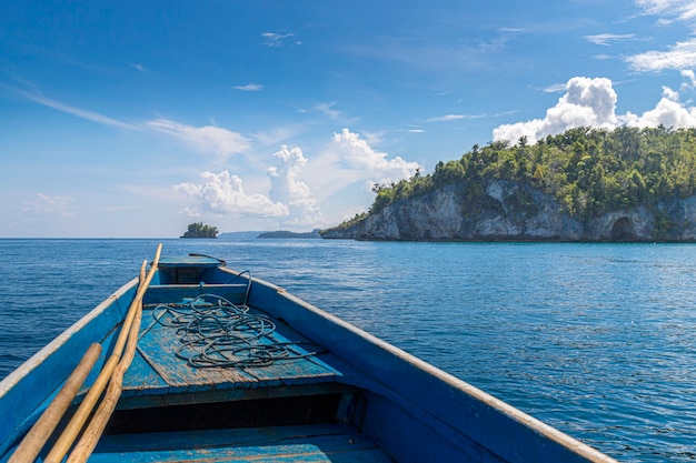 Bateau bleu rudimentaire au milieu de la mer devant une petite île, concept de voyage