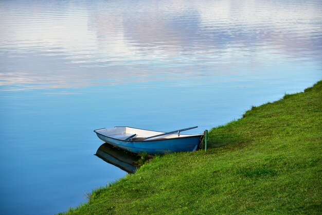 Bateau bleu solitaire au bord d'un lac calme.