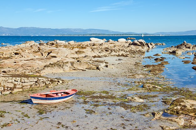 Bateau en bois sur la plage sablonneuse et rocheuse sous le ciel bleu