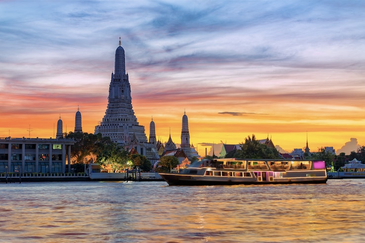 Photo bateau de croisière sur la rivière chao phraya avec temple de l'aube, wat arun, au coucher du soleil en arrière-plan, à l'horizontale