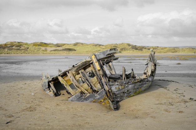 Photo bateau endommagé sur la plage contre un ciel nuageux