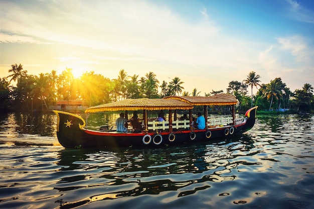 Bateau indien traditionnel .Kerala, les touristes se détendent sur un bateau le soir sur fond de beau coucher de soleil et de palmiers naturels. le tramway fluvial transporte les passagers à travers les canaux d'Alleppey.