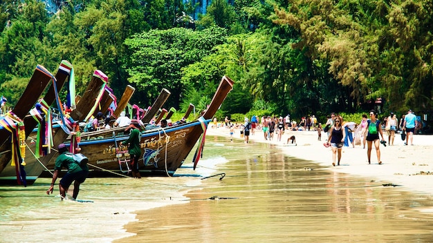 Un bateau longtail est amarré sur la plage en face d'une plage avec des gens qui marchent dessus.